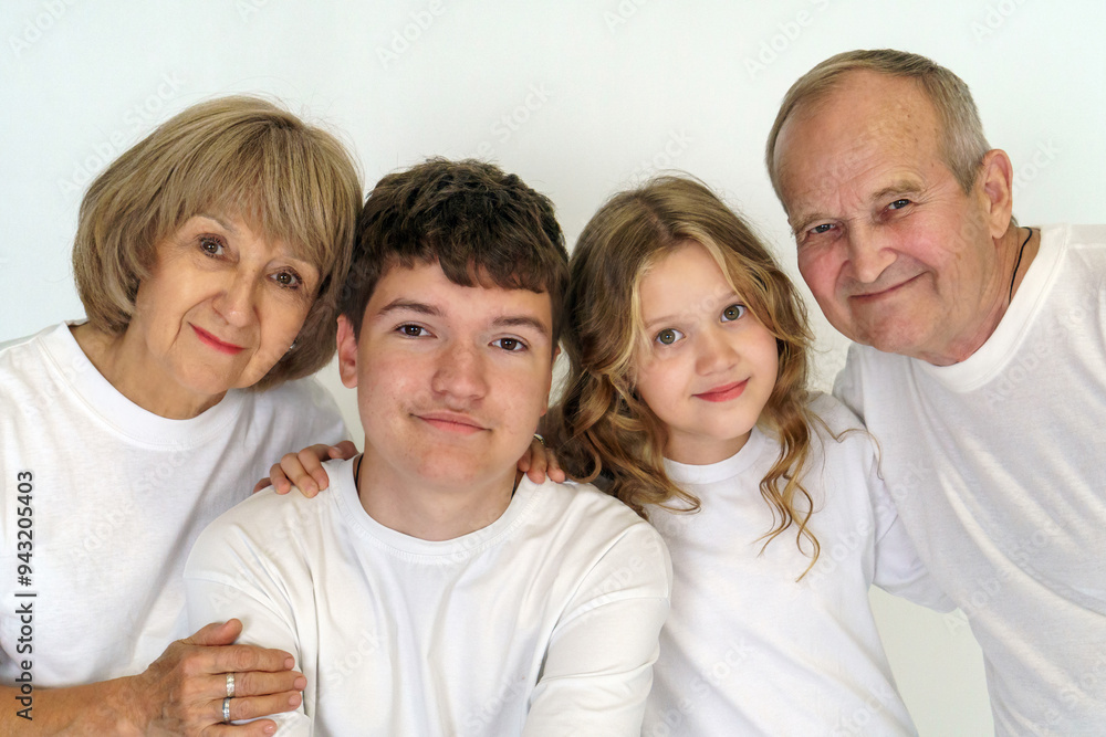 Happy family portrait with a loving elderly couple hugging their laughing young granddaughter and grandson while posing on white background. Space for text, studio photo. Happy family portrait with a loving elderly couple hugging their laughing young granddaughter and grandson while posing on white background. Space for text, studio photo.