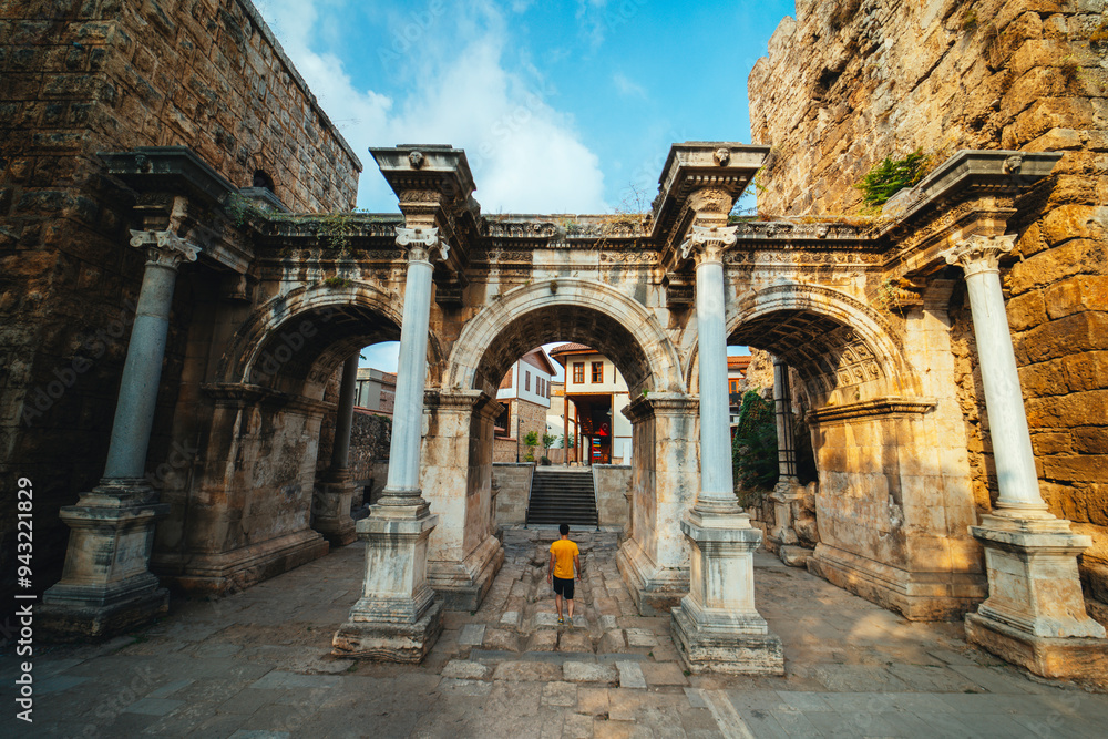 Obraz premium Hadrian's Gate. The three gates that are the symbol of Antalya. A man walks towards the gates. Wide angle photo taken on a cloudy day. Turkey.