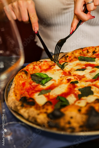 Cliente di una pizzeria elegante mentre taglia al tavolo un pizza margherita tradizionale con sugo di pomodoro, mozzarella e basilico fresco photo