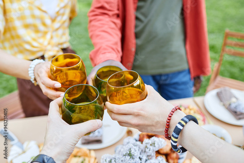 Group of friends clinking glasses together during outdoor gathering with food and greenery visible in background creating cheerful ambiance photo