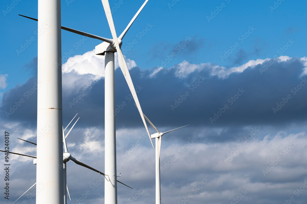 A close-up view of several wind turbines with their blades spinning, set against a dramatic backdrop of dark clouds, highlighting renewable energy and industrial design in Tarragona Spain A close-up view of several wind turbines with their blades spinning, set against a dramatic backdrop of dark clouds, highlighting renewable energy and industrial design in Tarragona Spain