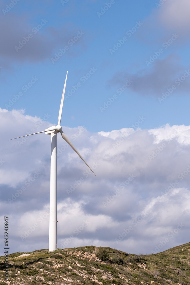 A lone wind turbine atop a hill stands against a background of dynamic clouds, representing both the isolation and the power of harnessing renewable energy in nature in Tarragona Spain A lone wind turbine atop a hill stands against a background of dynamic clouds, representing both the isolation and the power of harnessing renewable energy in nature in Tarragona Spain