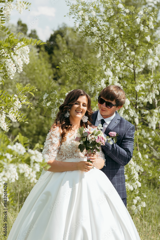 A bride and groom are posing for a picture in a field of white flowers. The bride is wearing a white dress and the groom is wearing a blue suit. They are both smiling and holding a bouquet of flowers A bride and groom are posing for a picture in a field of white flowers. The bride is wearing a white dress and the groom is wearing a blue suit. They are both smiling and holding a bouquet of flowers