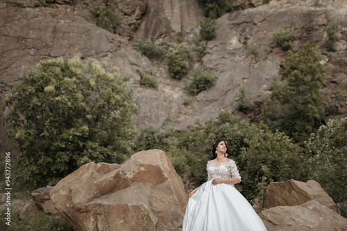 A woman in a white dress stands on a rocky hillside. The scene is serene and peaceful, with the woman posing for a photo in front of the natural beauty of the landscape