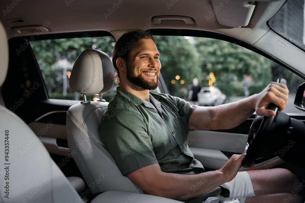 Happy man driving a car with a confident smile in a comfortable interior surrounded by greenery Happy man driving a car with a confident smile in a comfortable interior surrounded by greenery