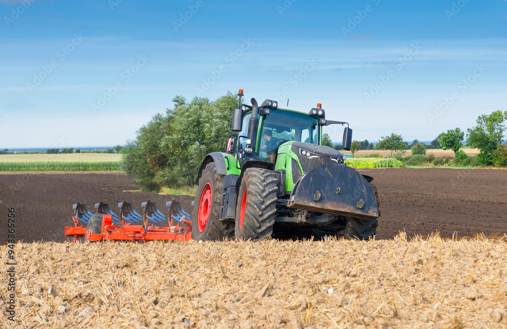 Obraz premium Tractor with 7-share reversible plow cultivating the field after the grain harvest - 2144