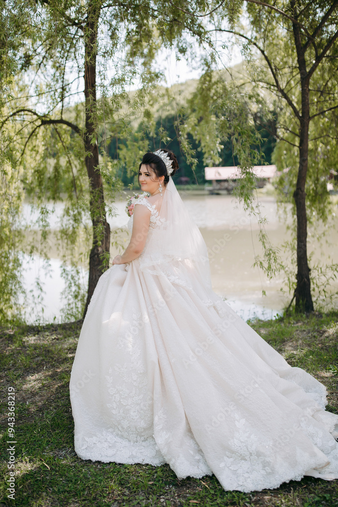 A woman in a white dress is standing in front of a body of water. She is wearing a veil and a headband A woman in a white dress is standing in front of a body of water. She is wearing a veil and a headband