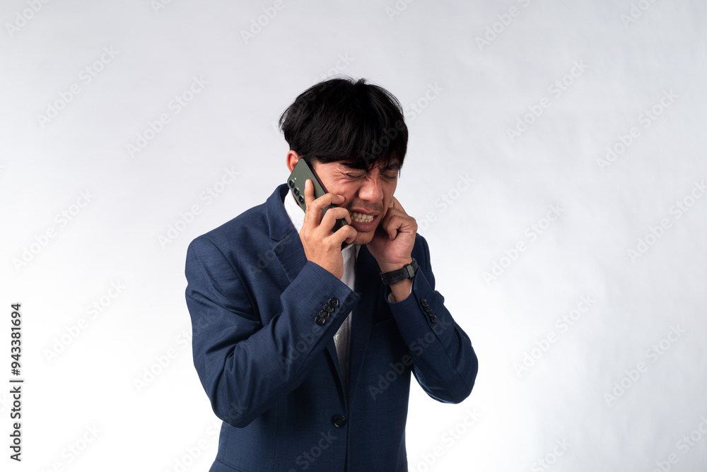 A surprised Asian businessman in a navy blue suit holds a smartphone to his ear, reacting with shock during a phone call. The white background emphasizes his expression A surprised Asian businessman in a navy blue suit holds a smartphone to his ear, reacting with shock during a phone call. The white background emphasizes his expression