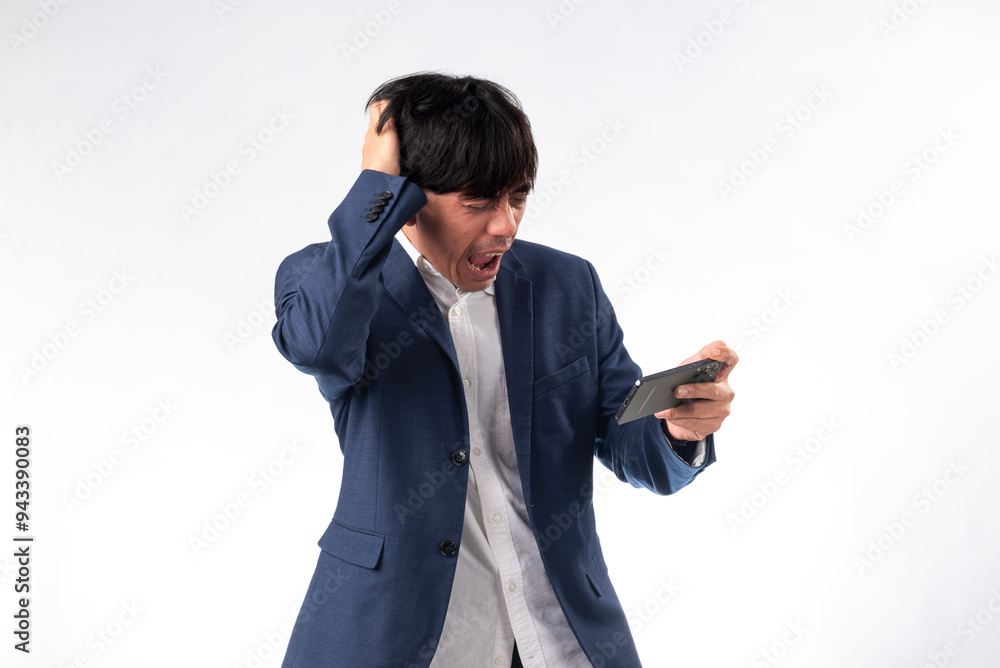 An Asian man in a blue suit expresses shock and frustration while looking at his smartphone, with a hand on his head. He stands against a plain white background, enhancing the emotional intensity An Asian man in a blue suit expresses shock and frustration while looking at his smartphone, with a hand on his head. He stands against a plain white background, enhancing the emotional intensity