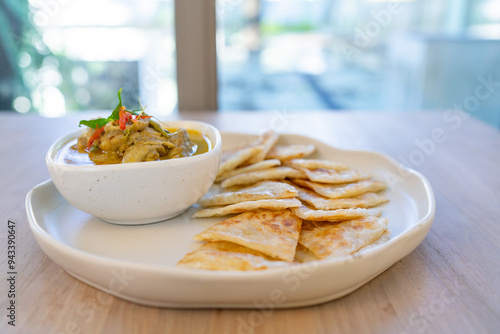 Crispy roti served with green curry with chicken on wooden table