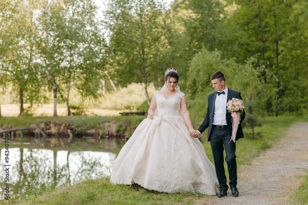 A bride and groom are walking down a path near a pond. The bride is wearing a long white dress and the groom is wearing a black suit. They are holding hands A bride and groom are walking down a path near a pond. The bride is wearing a long white dress and the groom is wearing a black suit. They are holding hands