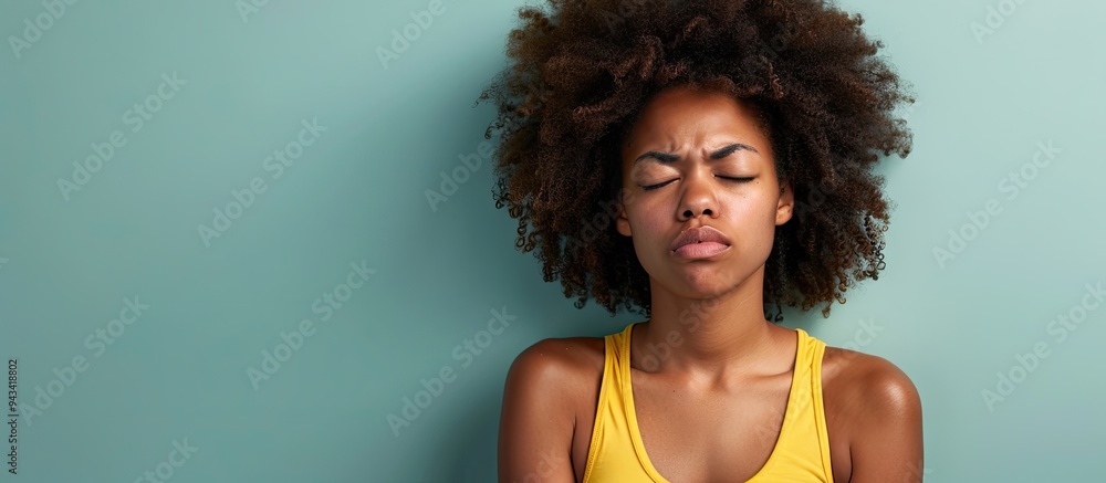 African American woman wearing a yellow tank top looks unwell with closed eyes rubbing her nose set against a plain pastel green studio background with copy space image African American woman wearing a yellow tank top looks unwell with closed eyes rubbing her nose set against a plain pastel green studio background with copy space image