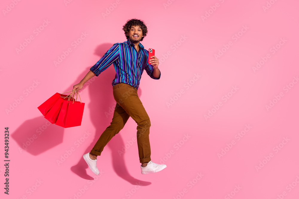 Full size photo of nice young man jump run phone bags empty space wear shirt isolated on pink color background Full size photo of nice young man jump run phone bags empty space wear shirt isolated on pink color background