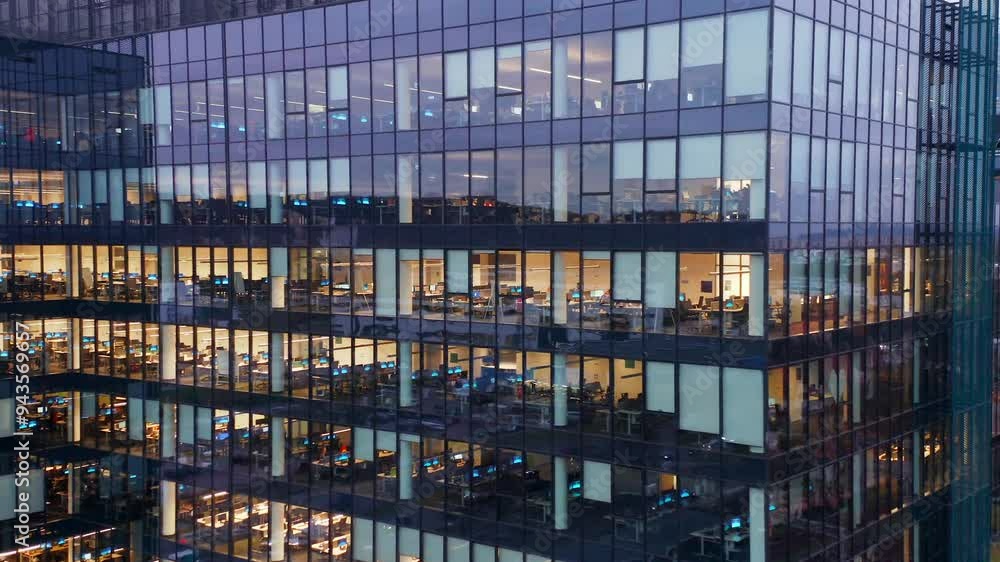 A panoramic drone shot captures the illuminated windows a modern glass skyscraper, where business professionals are seen working late into the night, reflecting the high-pressure corporate lifestyle A panoramic drone shot captures the illuminated windows a modern glass skyscraper, where business professionals are seen working late into the night, reflecting the high-pressure corporate lifestyle