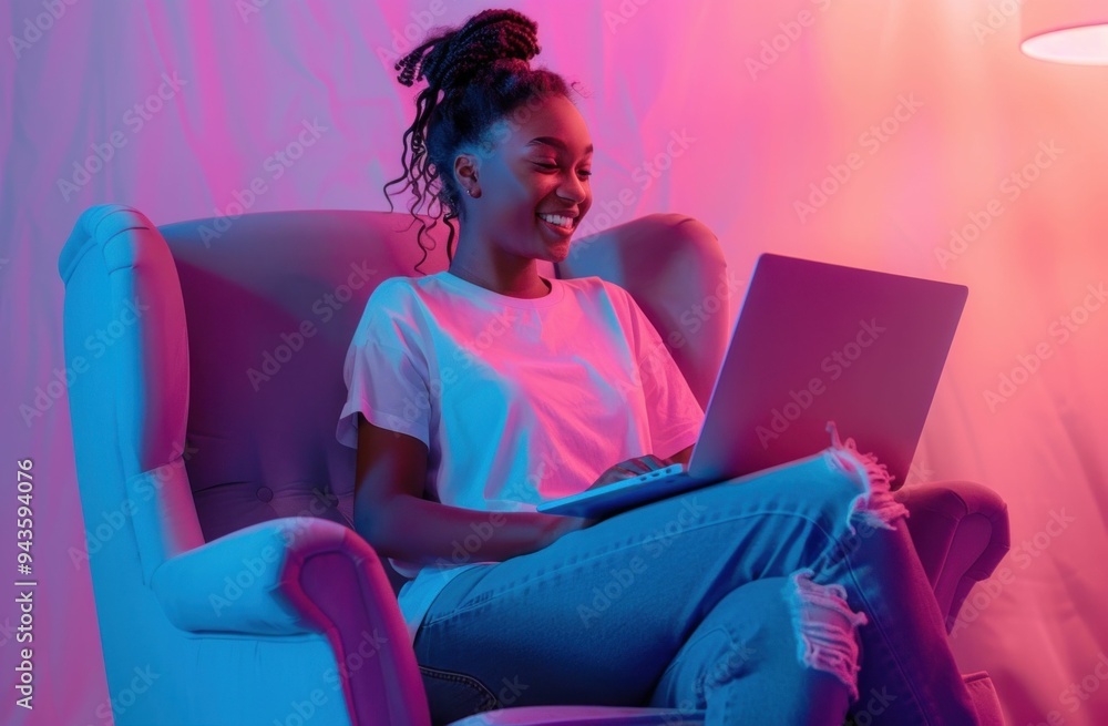 Woman working on a laptop while sitting in a cozy armchair with colorful lighting in the background Woman working on a laptop while sitting in a cozy armchair with colorful lighting in the background