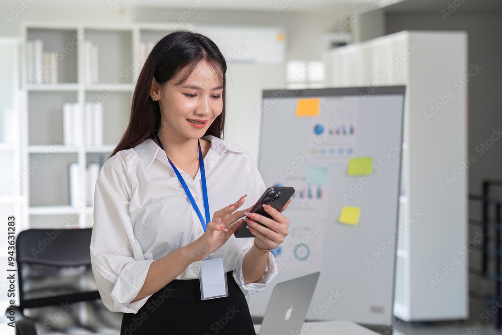Young Accountant Using Smartphone in Modern Office Setting with Charts and Laptop in Background Young Accountant Using Smartphone in Modern Office Setting with Charts and Laptop in Background