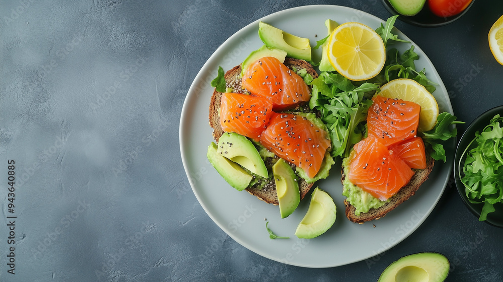Overhead Shot of Healthy Salmon Avocado Toast. Overhead view of smoked salmon avocado toast on a plate with greens and lemon. Overhead Shot of Healthy Salmon Avocado Toast. Overhead view of smoked salmon avocado toast on a plate with greens and lemon.