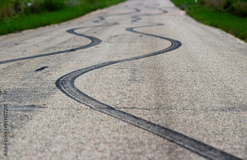 фотографія Low angle close up of curved black tire skid marks winding down an asphalt country road, showcasing dramatic rubber tracks from reckless driving, drifting, or braking