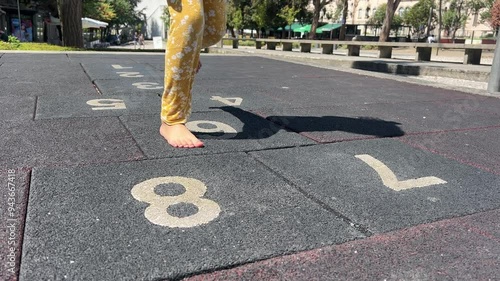 Child girl playing barefoot on numbered hopscotch tiles at an outdoor playground photo