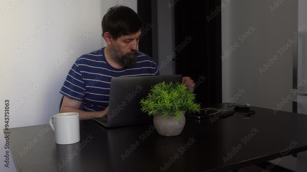A person working at home on a laptop answers a phone call. A person working at home on a laptop answers a phone call.