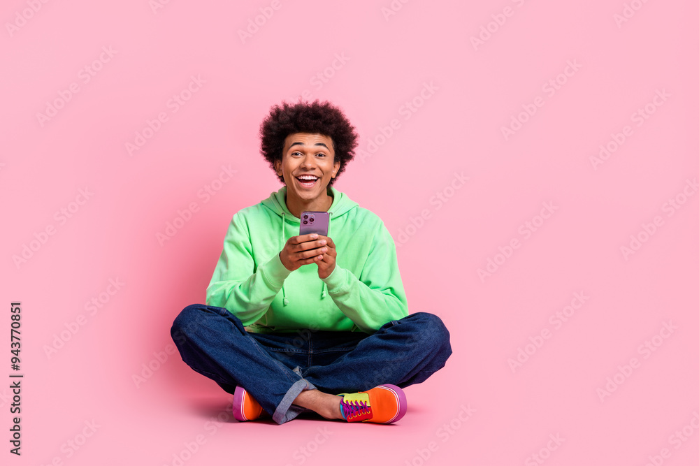 Full body portrait of cool young man sit floor phone wear green hoodie isolated on pink color background Full body portrait of cool young man sit floor phone wear green hoodie isolated on pink color background