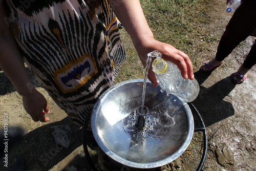 woman in national uzbek dress fills plastic bottle with water, central asian region water problem photo