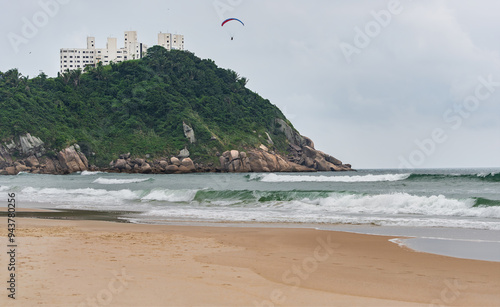 The Tombo Beach of Guaruja, SP, Brazil. The view of the beach with no people, hills in the background, and a paraglider flying in the sky.