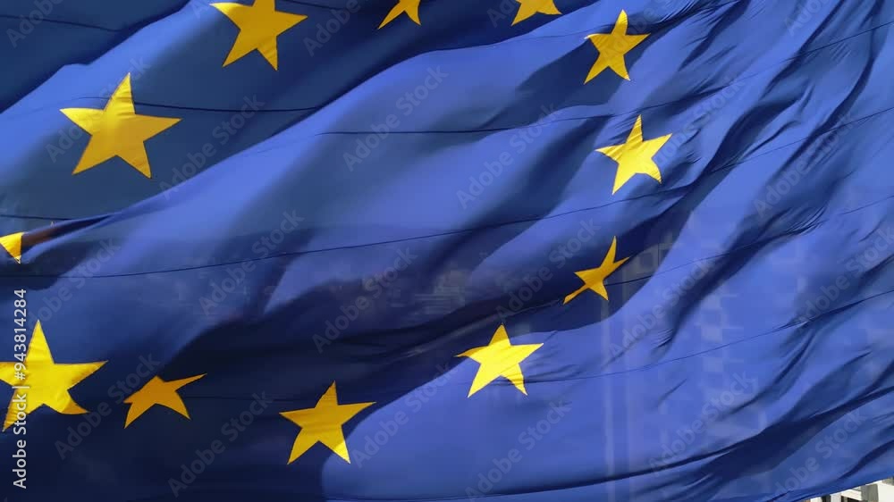 A close-up shot of the European Union flag waving in the wind, with its iconic blue background and golden stars. The movement of the fabric adds a dynamic and patriotic feel A close-up shot of the European Union flag waving in the wind, with its iconic blue background and golden stars. The movement of the fabric adds a dynamic and patriotic feel