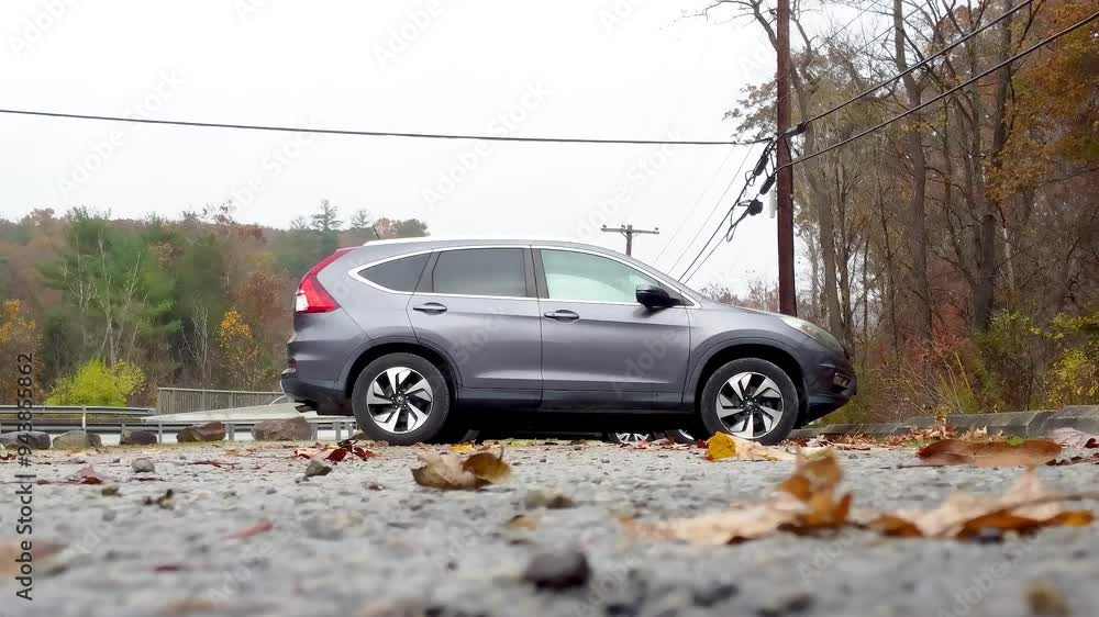 low angle view of car parked on road over yellow autumn leaves in cloudy day. Colorful autumn foliage flies out from under wheel of automobile. SUV parked on empty road in ohiopyle state park in fall