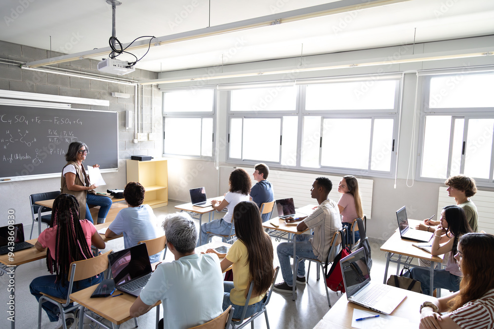 Obraz premium High angle view of mature female teacher explaining lesson to multiracial high school students in class.