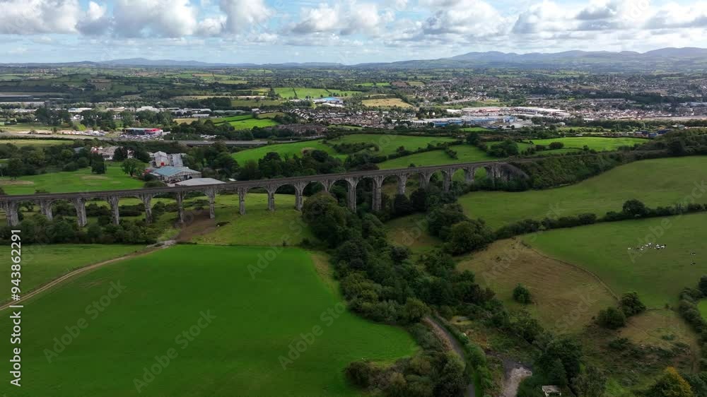 Craigmore Viaduct, County Armagh, Northern Ireland, September 2022. Drone orbits slowly around the Victorian Railway Bridge over green pasture with Newry town under an overcast sky. Craigmore Viaduct, County Armagh, Northern Ireland, September 2022. Drone orbits slowly around the Victorian Railway Bridge over green pasture with Newry town under an overcast sky.