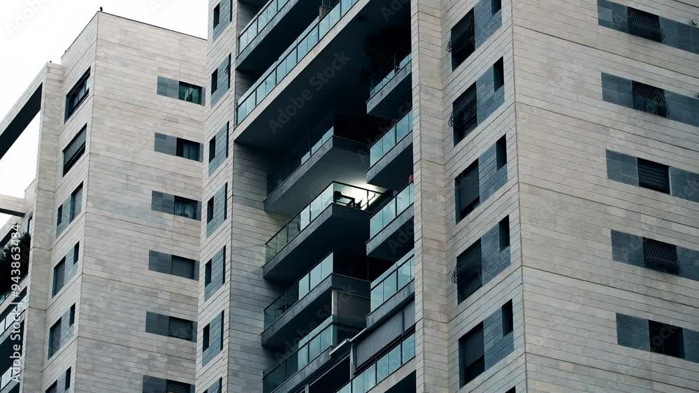 A semi telephoto clip showing a part of a 10-15 stories residential building, with balconies and windows. all stories are dark, except one balcony, that has a light turned on. A semi telephoto clip showing a part of a 10-15 stories residential building, with balconies and windows. all stories are dark, except one balcony, that has a light turned on.