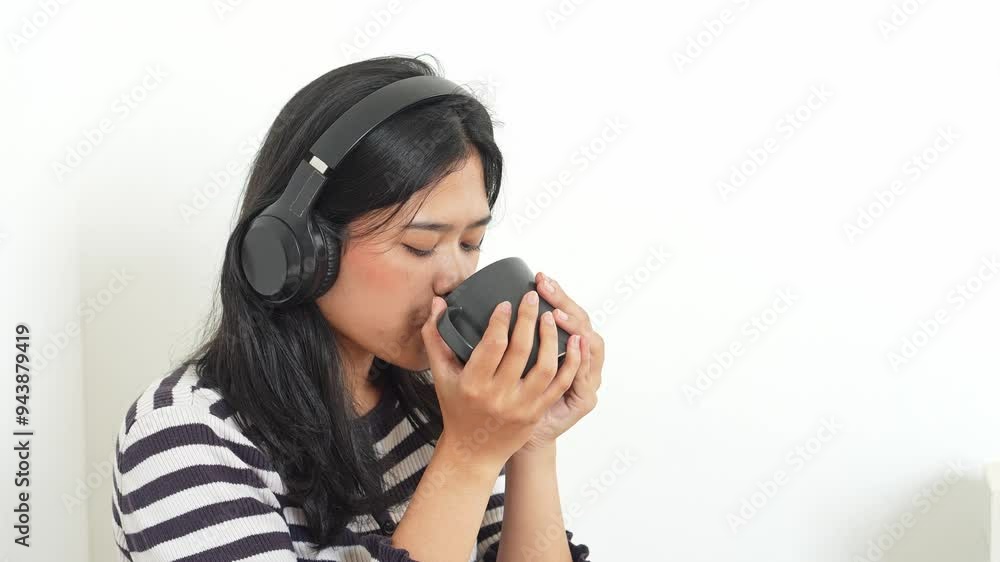 Young Asian Woman Enjoying Music While Blowing Hot Tea On Mug Young Asian Woman Enjoying Music While Blowing Hot Tea On Mug