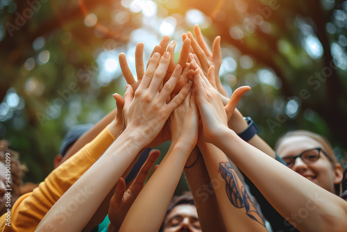 A group of people giving a collective high five outdoors, symbolizing unity, teamwork, and celebration of success, with sunlight filtering through the trees photo