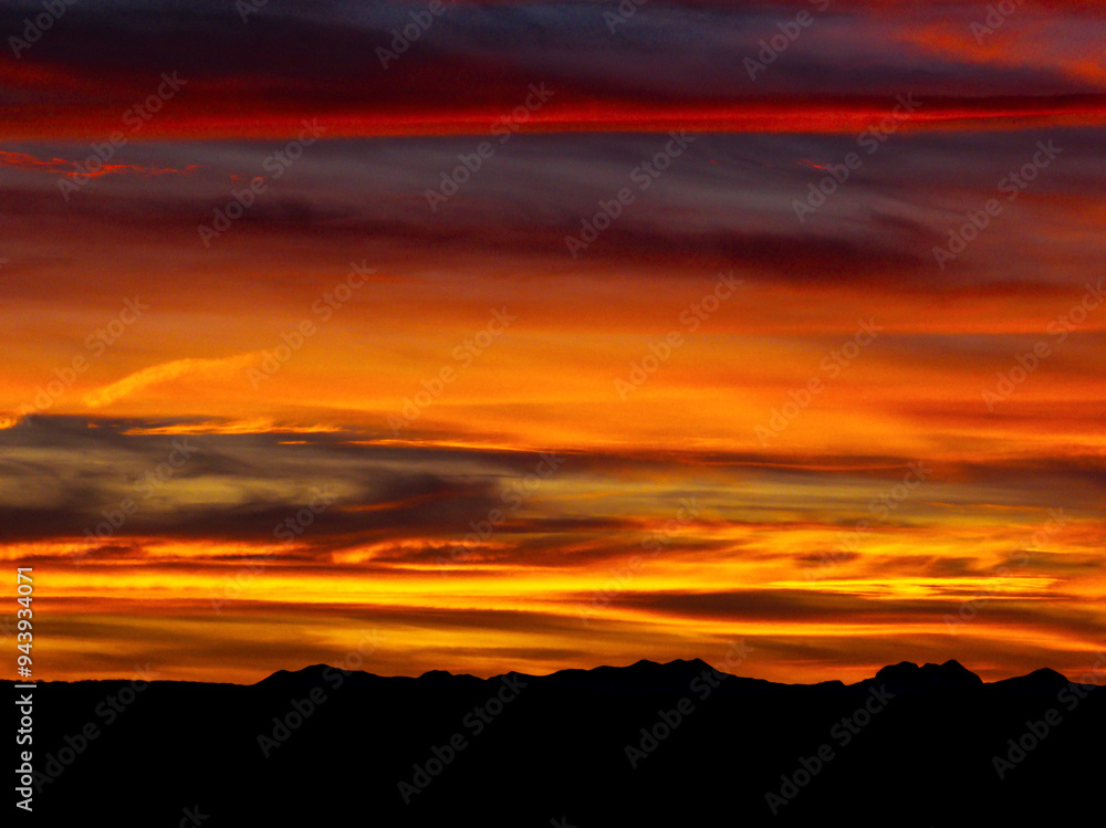 Colorful red and gold clouds in a dramatic sky with a silhouetted mountain range; Calgary, Alberta, Canada Colorful red and gold clouds in a dramatic sky with a silhouetted mountain range; Calgary, Alberta, Canada