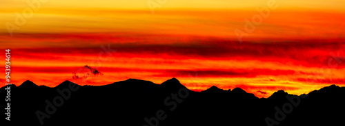 Panoramic of dramatic, colorful red and gold sky with a silhouetted mountain range; Calgary, Alberta, Canada