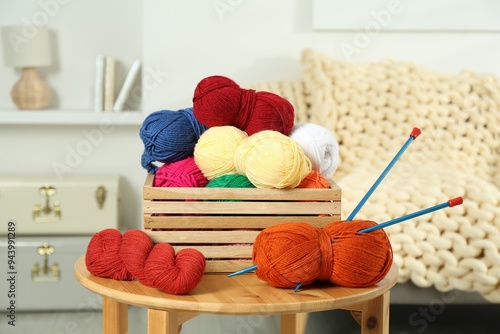 Skeins of soft yarn in crate and knitting needles on wooden table indoors photo