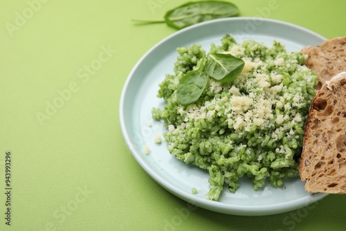 Tasty spinach risotto and bread on light green background, closeup. Space for text