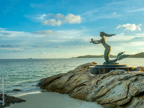 Mermaid sculpture in outdoor public sand and rock beach with seascape view at Samet island, Rayong, Thailand, under twilight sunset cloudy sky