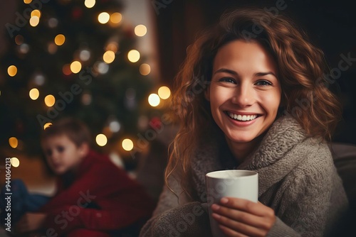 Smiling woman enjoys a cozy moment by the Christmas tree, holding a warm cup, illuminated by festive lights.