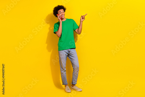 Full length photo of funky cool guy dressed green t-shirt talking modern gadget pointing emtpy space isolated yellow color background