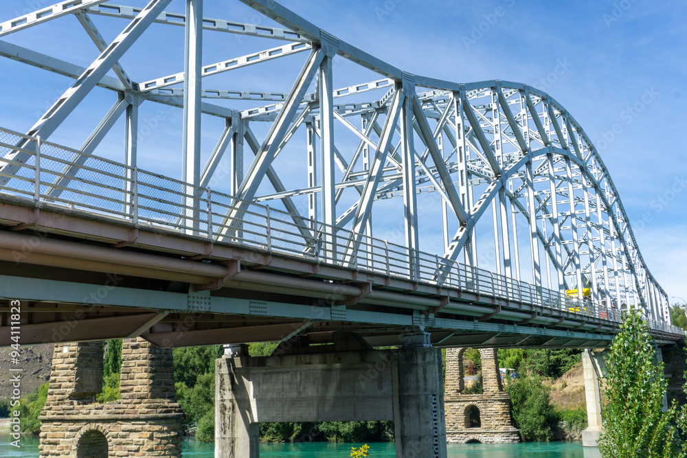 Fototapeta premium Historic bridge ruins over the Clutha River in Alexandra, New Zealand. Surrounded by the striking blue waters and lush greenery of Otago, nature lovers photographers exploring South Island