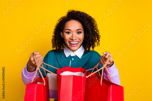 Photo portrait of lovely young lady peek look shopping bags dressed stylish striped garment isolated on yellow color background