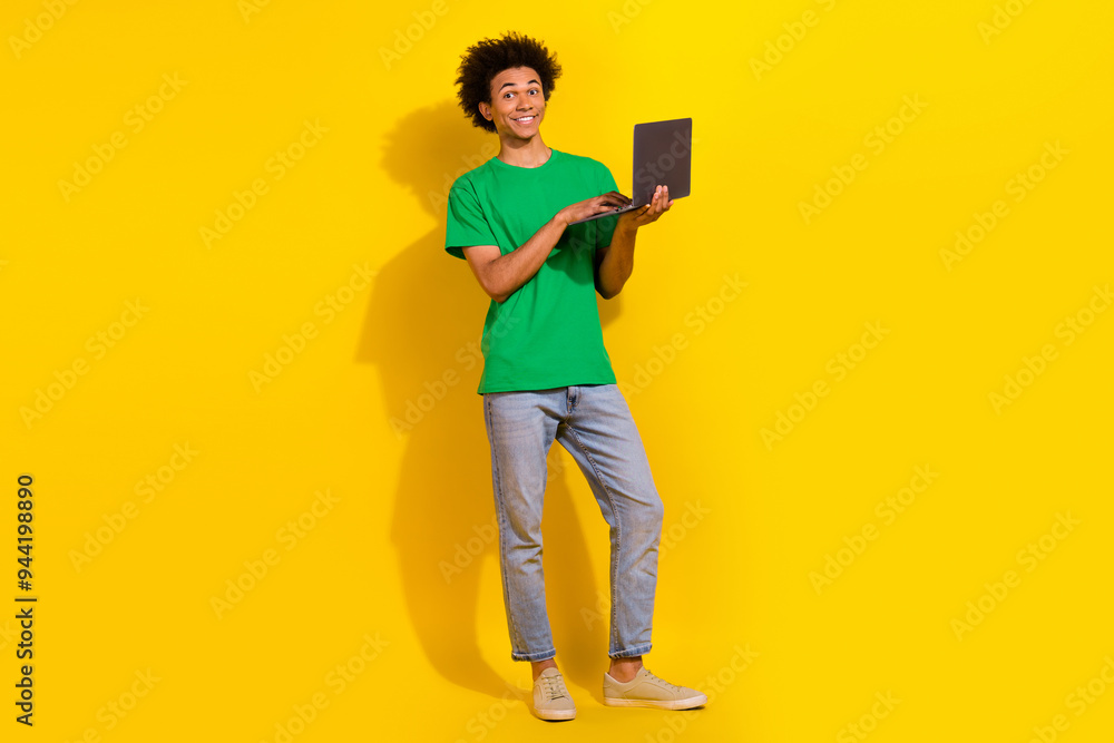 Full length photo of cheerful positive guy dressed green t-shirt working modern device emtpy space isolated yellow color background Full length photo of cheerful positive guy dressed green t-shirt working modern device emtpy space isolated yellow color background