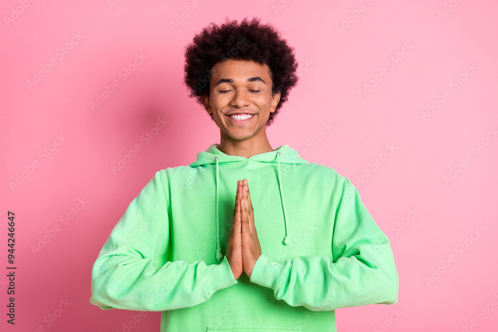 Portrait of nice young man closed eyes pray meditate wear green hoodie isolared on pink color background Portrait of nice young man closed eyes pray meditate wear green hoodie isolared on pink color background
