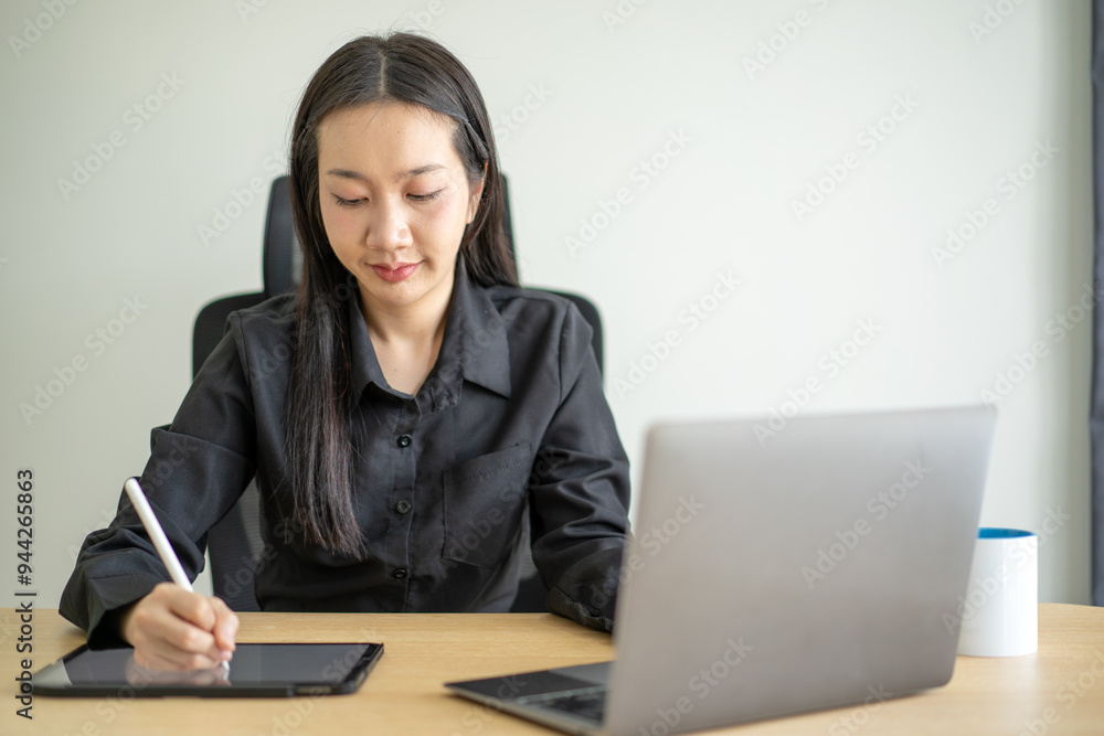 A woman is sitting at a desk with a laptop and a tablet A woman is sitting at a desk with a laptop and a tablet