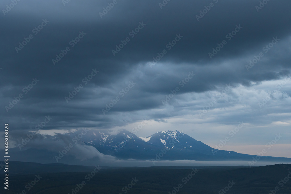 Beautiful evening landscape. View of the volcanoes at dusk. Overcast weather. Low clouds. The epic nature of the Kamchatka Peninsula. Travel and tourism in Siberia and the Russian Far East. Kamchatka. Beautiful evening landscape. View of the volcanoes at dusk. Overcast weather. Low clouds. The epic nature of the Kamchatka Peninsula. Travel and tourism in Siberia and the Russian Far East. Kamchatka.