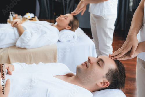 Caucasian couple enjoying relaxing anti-stress head massage and pampering facial beauty skin recreation leisure in dayspa modern light ambient at luxury resort or hotel spa salon. Quiescent