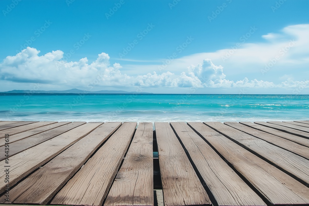 An empty wooden deck stretches out towards a bright, clear blue ocean under a sunny sky with scattered clouds in view. An empty wooden deck stretches out towards a bright, clear blue ocean under a sunny sky with scattered clouds in view.