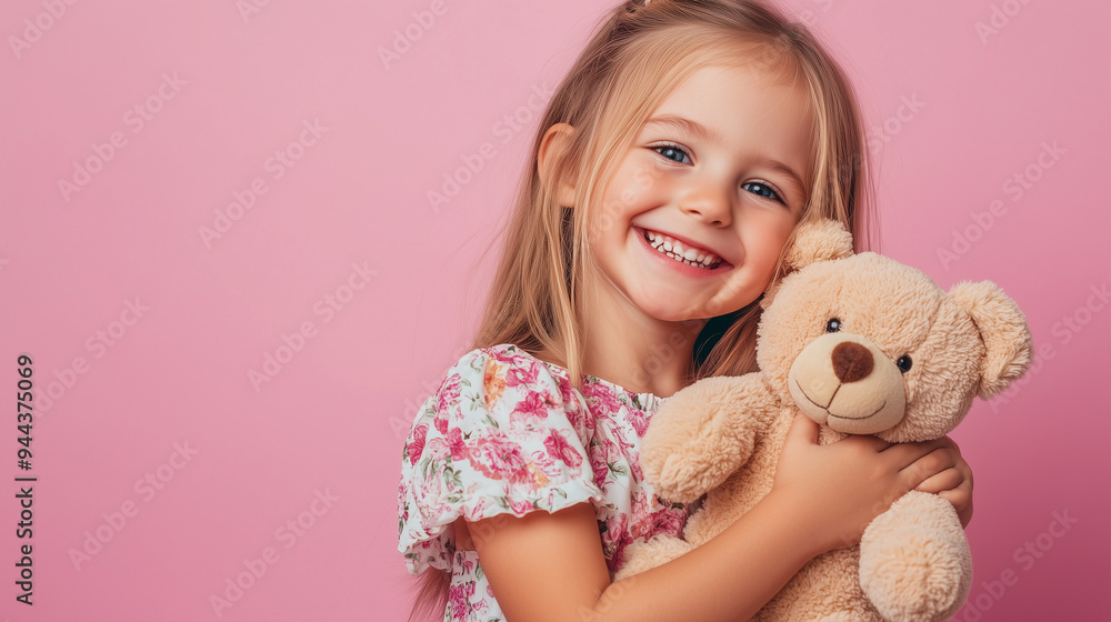 Portrait of happy young girl in floral dress holding a teddy bear and smiling brightly against a pastel pink background Portrait of happy young girl in floral dress holding a teddy bear and smiling brightly against a pastel pink background